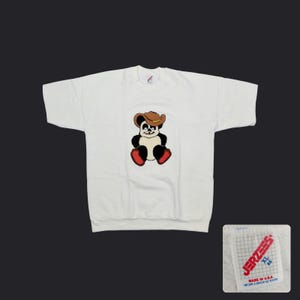 May include: White sweatshirt featuring a cartoon panda wearing a cowboy hat and red boots. The panda is embroidered on the front. The tag in the lower right corner reads "Jerzees" and "Made in U.S.A."