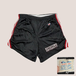 May include: Black athletic shorts with red and white side stripes. The shorts feature the text "Kutztown University" in white and a Champion logo. The tag indicates a size small and a waist size of 28-30 inches.