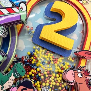 Puede incluir: Decoraci&oacute;n colorida y en capas con personajes de la pel&iacute;cula Toy Story. El dise&ntilde;o incluye un gran n&uacute;mero 2 amarillo, un arco iris y recortes de personajes, con acentos amarillos, rojos y azules. El fondo tiene un patr&oacute;n de cielo y nubes.