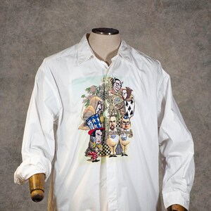 May include: A white long-sleeve button-down shirt featuring a central graphic print of various cartoon characters, including a figure in a tall red, white, and blue striped hat, alongside other stylized figures and a spade playing card symbol.