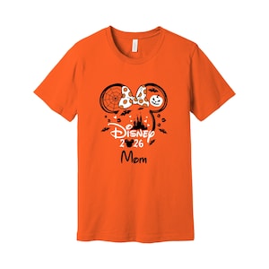 May include: Orange t-shirt with a Disney Halloween design. The design includes Mickey Mouse ears, a bow, a castle silhouette, bats, and the text "Disney 2026 Mom."