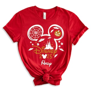 May include: Red t-shirt with a Halloween-themed Disney design. The design includes Mickey Mouse ears with a spiderweb and jack-o'-lantern, bats, a castle, and the text "Disney 2025" with a name below.