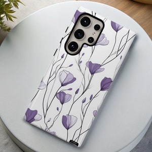 May include: A white phone case with a floral design featuring purple flowers and black stems. The case has a camera cutout with a black border.