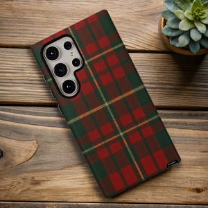 May include: A phone case with a red, green, and yellow plaid pattern. The case is on a wooden surface. The phone case has a camera module with multiple lenses.