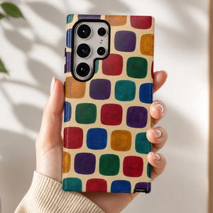 May include: A rectangular smartphone case featuring a repeating pattern of rounded squares in shades of red, blue, green, purple, and gold against a cream background, with a black camera module cutout positioned at the top left corner.