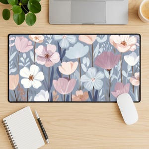 May include: A rectangular desk mat featuring a repeating pattern of stylized flowers in shades of dusty pink, soft blue, and white against a muted gray-blue background. The floral design includes various petal shapes, thin stems, and leaves.