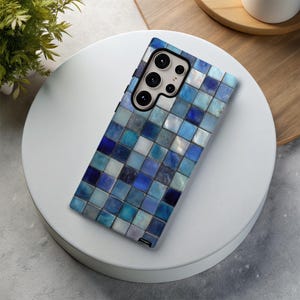 May include: A smartphone case with a mosaic tile design in shades of blue, white, and gray. The case has a rectangular shape with a camera cutout and buttons. The design is made up of small, square tiles.