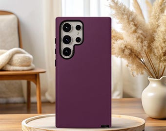 May include: A plum-colored phone case with a camera module cutout. The case has a smooth, matte finish and a rectangular shape. The phone case is displayed on a wooden tray.