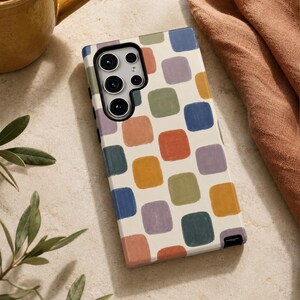 May include: A rectangular smartphone case featuring a cream-colored background with a repeating pattern of rounded squares in muted shades of terracotta, sage green, dusty blue, mustard yellow, and lavender, with a black camera cutout section.