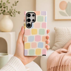 May include: A rectangular smartphone case featuring a repeating pattern of rounded squares in pastel shades of yellow, pink, blue, green, and lavender against a cream background. The case has a black camera cutout section at the top left corner.
