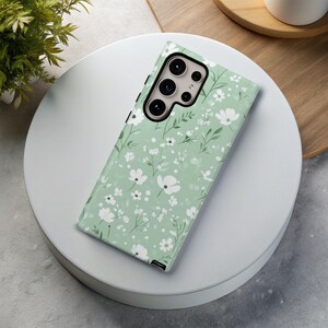 May include: A green phone case with a white floral pattern. The case has a cutout for the camera lens.