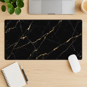 May include: A rectangular black mouse pad with a gold marble design. The mouse pad is on a light wood surface, with a laptop, a white mouse, a notepad, a pen, and a small plant visible.