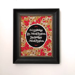 Może przedstawiać: Wydruk w ramie z czarnym tłem i białym kołem w środku. Koło zawiera tekst "Everything In Moderation Including Moderation" w białym, stylizowanym foncie. Tło wydruku to czerwony i biały wzór kwiatowy.