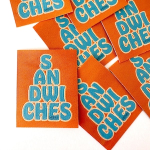 May include: Several orange fabric patches with the text "SANDWICHES" in blue stacked on top of each other.