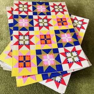May include: A stack of fabric squares with a repeating pattern of red, blue, yellow, and pink stars. The fabric is a cream color with a subtle texture.