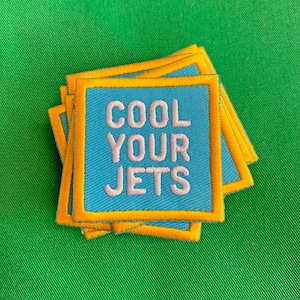 May include: A stack of blue and yellow fabric patches with the text "COOL YOUR JETS" in white embroidery.