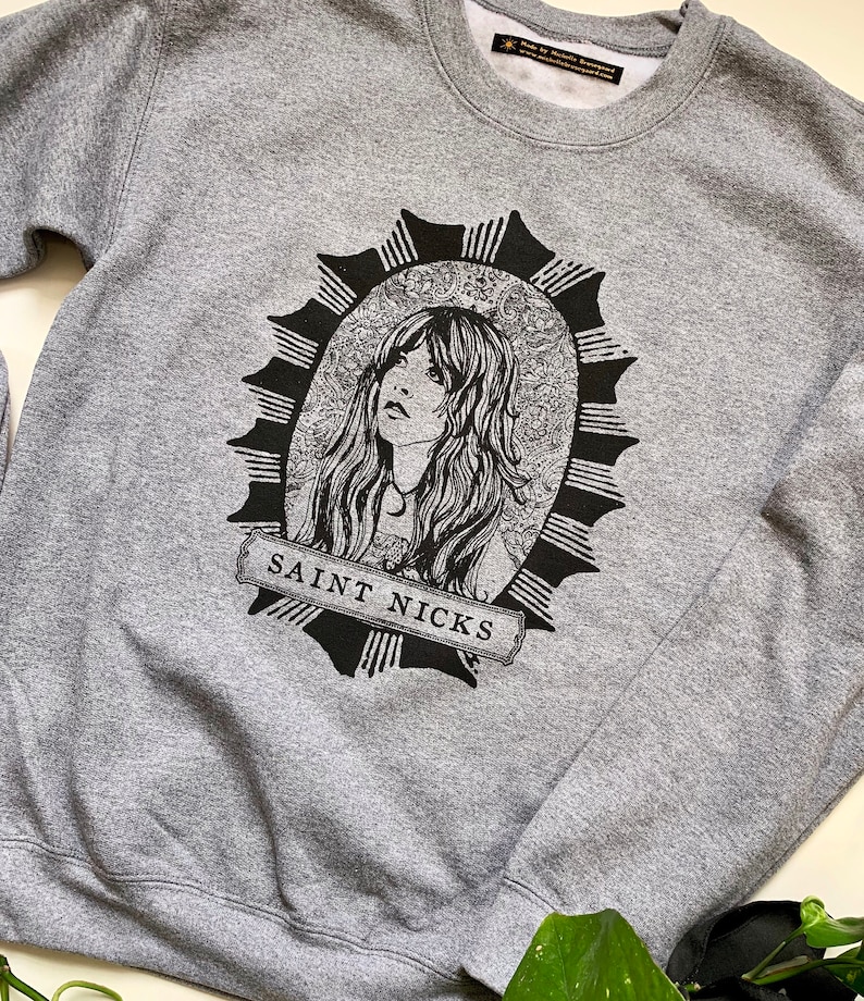May include: Grey sweatshirt with a black and white illustration of a woman with long hair in a circular frame with the text "SAINT NICKS" at the bottom.