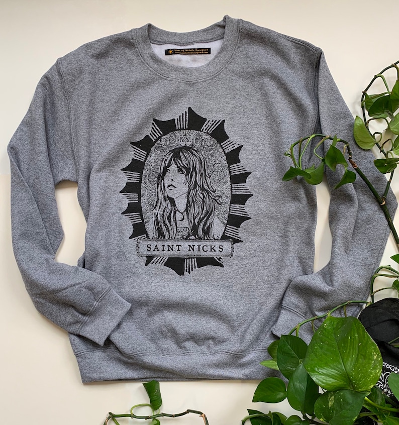 May include: Grey sweatshirt with a black and white graphic print of a woman's face in a circle with the text "SAINT NICKS" below.