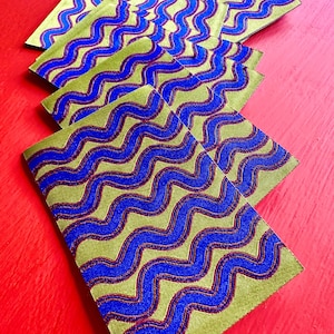May include: Several rectangular fabric pieces with a repeating wavy pattern in blue and red on a green background. The fabric pieces are arranged on a red surface, creating a visually appealing contrast.