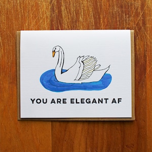 Könnte beinhalten: Ein weißer Schwan mit orangefarbenem Schnabel schwimmt in blauem Wasser. Der Text "YOU ARE ELEGANT AF" ist unter dem Schwan gedruckt.