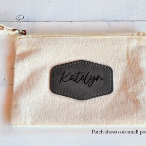 May include: A small, off-white canvas pouch with a zipper closure. A gray leather patch with the name "Katelyn" is sewn onto the front of the pouch. Patch shown on small pouch.