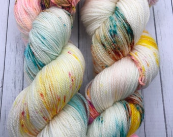 Puede incluir: Dos ovillos de hilo blanco con motas de color rosa, amarillo, azul y marrón. El hilo es suave y esponjoso, perfecto para tejer o hacer ganchillo.
