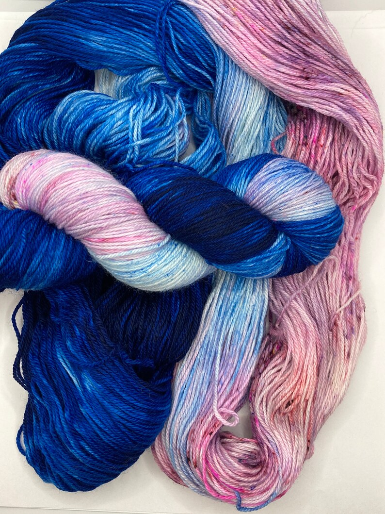May include: Two skeins of yarn, one blue and one pink, with a white and blue ombre effect. The yarn is soft and fluffy, perfect for knitting or crocheting.