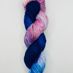 May include: A skein of yarn with a gradient of blue, pink, and white colors. The yarn is twisted into a spiral shape.