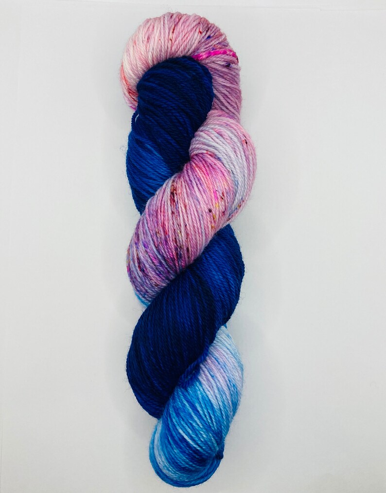 May include: A skein of yarn with a gradient of blue, pink, and white colors. The yarn is twisted into a spiral shape.