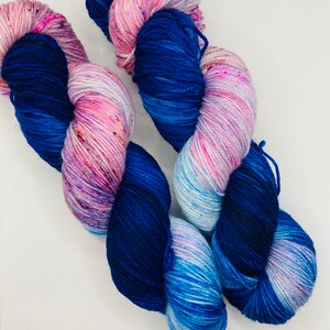 May include: Two skeins of yarn, one blue and white with pink speckles, the other a deep blue with pink and white speckles.