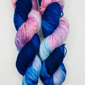 May include: Two skeins of yarn in a blue, pink, and white colorway. The yarn is a variegated blend with speckles of color throughout.