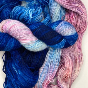 May include: Three skeins of yarn in shades of blue, pink, and white. The yarn is soft and fluffy, and it would be perfect for knitting or crocheting.