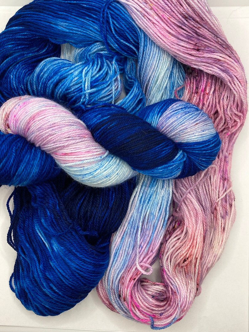 May include: Three skeins of yarn in shades of blue, pink, and white. The yarn is soft and fluffy, and it would be perfect for knitting or crocheting.