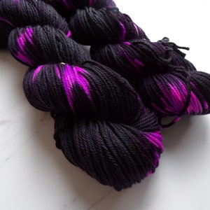 Puede incluir: Primer plano de varios ovillos de lana. La lana es de un negro intenso con vibrantes vetas magenta. La textura de la lana es visible, lo que sugiere un material suave, posiblemente de lana. Los ovillos están dispuestos en un montón suelto y natural.