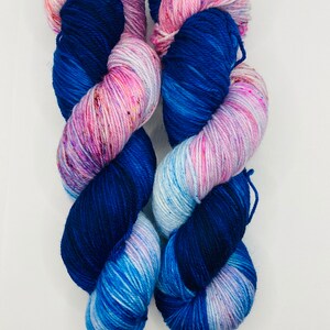 May include: Two skeins of yarn in shades of blue, pink, and white. The yarn is hand-dyed and has a speckled appearance.