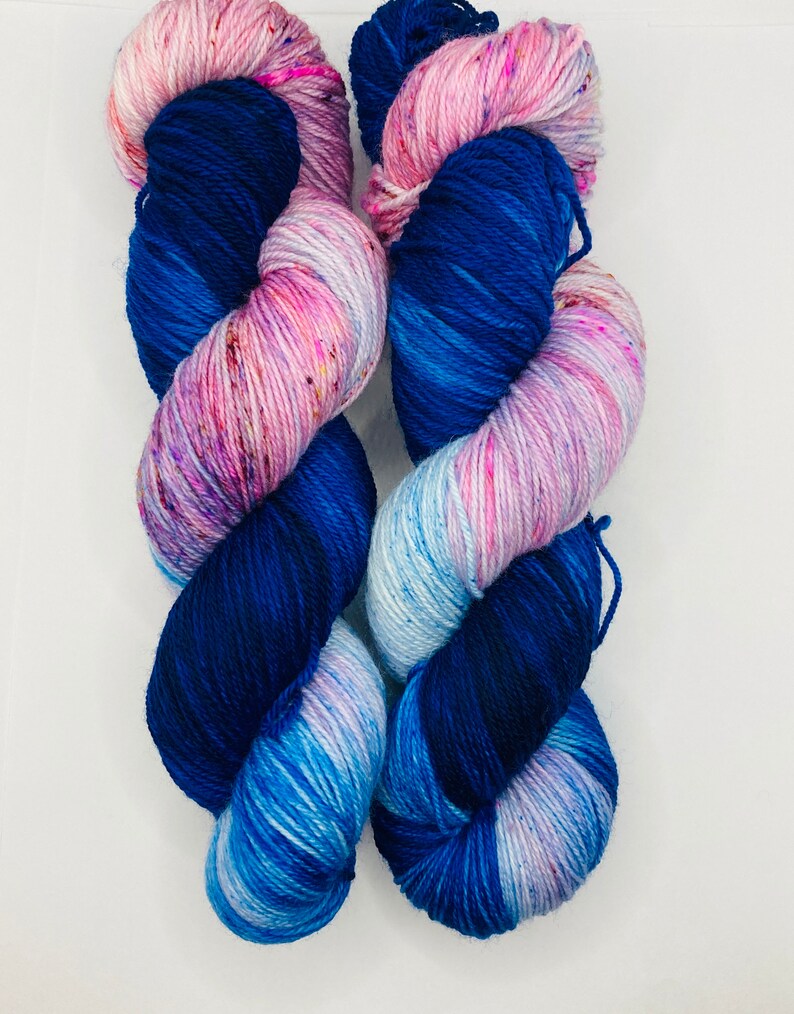 May include: Two skeins of yarn in shades of blue, pink, and white. The yarn is hand-dyed and has a speckled appearance.