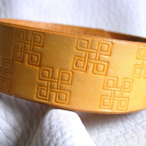 May include: A light brown leather bracelet with a repeating embossed pattern of interlocking squares.