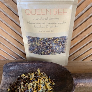 May include: A package of "QUEEN BEE" organic herbal tea/tisane. The ingredients include African honeybush, chamomile, lavender, lemon balm, and calendula. A wooden scoop holds a portion of the loose tea. The package is one ounce.