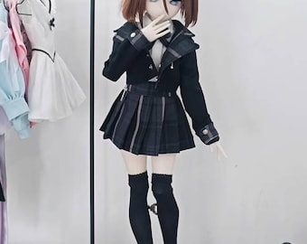 May include: A doll with brown hair and blue eyes, wearing a black school uniform with a pleated skirt and knee-high socks. The doll has bunny ears and is standing on a metal stand. A clothing rack is in the background.