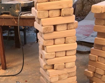 May include: A wooden tower game made of stacked blocks. The tower is tall and narrow, with the blocks arranged in a staggered pattern. The blocks are all made of natural wood and have a light brown color.