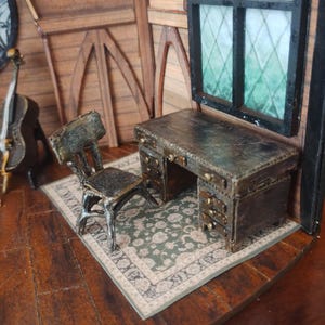 Puede incluir: Un escritorio de madera en miniatura con cajones y una silla se encuentra sobre una alfombra de patrones verdes y crema en una habitación de casa de muñecas. El escritorio es de color marrón oscuro con un acabado desgastado. La silla también es de color marrón oscuro con un diseño simple. La habitación tiene paredes de madera y una ventana con un diseño de vitral.