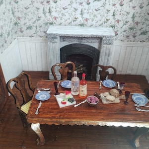 Puede incluir: Un juego de comedor de madera con cuatro sillas, una chimenea blanca y papel tapiz floral. La mesa está puesta con platos, cubiertos, vasos y comida. Hay dos botellas de vino en la mesa.