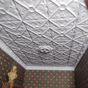 Könnte beinhalten: Eine weiße Decke mit einem dekorativen, geometrischen Muster. Die Decke besteht aus gepressten Blechteilen und hat ein zentrales Medaillon.