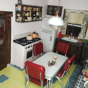 Pu&ograve; includere: Scena di cucina retr&ograve; in miniatura con una stufa rosa e bianca, un frigorifero bianco e un tavolo con sedie rosse. Una mensola espone cibi in miniatura. Un lampadario illumina la scena.