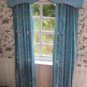 May include: A pair of blue curtains with a white floral pattern featuring birds. The curtains have a valance with the same pattern. The curtains are hung on a window with a white frame.