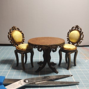 Puede incluir: Un juego de mesa de madera en miniatura con dos sillas. Las sillas tienen marcos dorados ornamentados y asientos de tela a rayas amarillas y blancas. La mesa tiene una tapa de madera marrón con un borde dorado y una base negra.