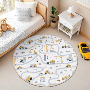 Puede incluir: Una alfombra redonda para niños con un diseño de construcción. La alfombra blanca presenta un diseño de carretera con vehículos de construcción amarillos, edificios y grúas. El borde es de color beige claro. Un coche de juguete amarillo está en el suelo.