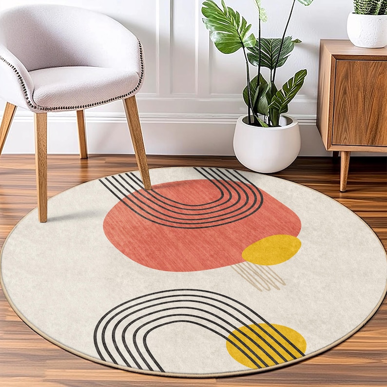 May include: A round cream-colored rug with a geometric design featuring black lines, red and yellow circles. The rug has a subtle fringe border.