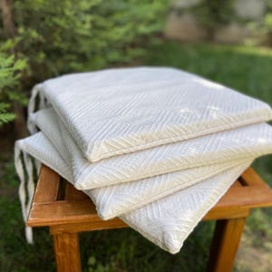 Puede incluir: Un conjunto de cuatro cojines de silla de algodón blanco con un patrón geométrico. Los cojines están sobre una silla de madera.