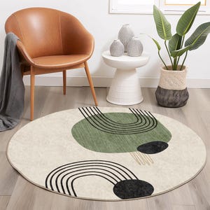 May include: A round, cream-colored rug with a green and black abstract design. The rug features two large, overlapping circles with black outlines and a series of black arches. The larger circle is green and the smaller circle is black.
